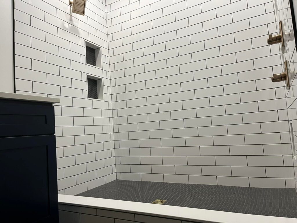 Shower with white subway tile walls, dark hexagonal floor tiles, built-in niches, and brass fixtures.