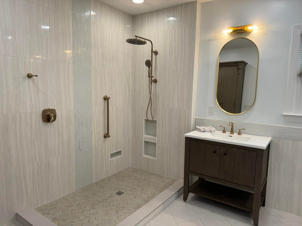 Spacious shower with light tile walls, gold fixtures, a glass accent strip, and a dark wood vanity with an oval mirror.