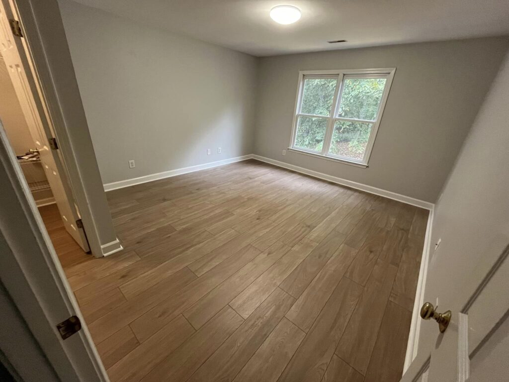 A bright, empty room with wood-look tile flooring.