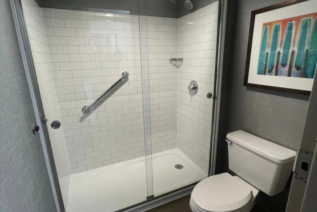 Compact bathroom with a glass-enclosed shower featuring white subway tiles, a stainless steel grab bar, and a wall-mounted toilet.